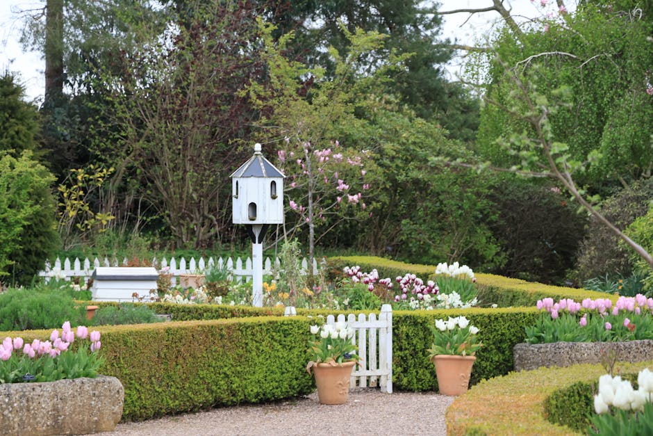 A close-up view of a yellow garden candle with a partially melted edge, positioned outdoors during twilight. In the background, a blurred garden scene with subtle greenery and soft natural light can b